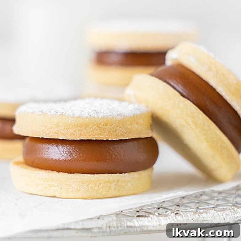 Two leaning shortbread dulce de leche cookies on a white paper and wire rack. Light grey background.