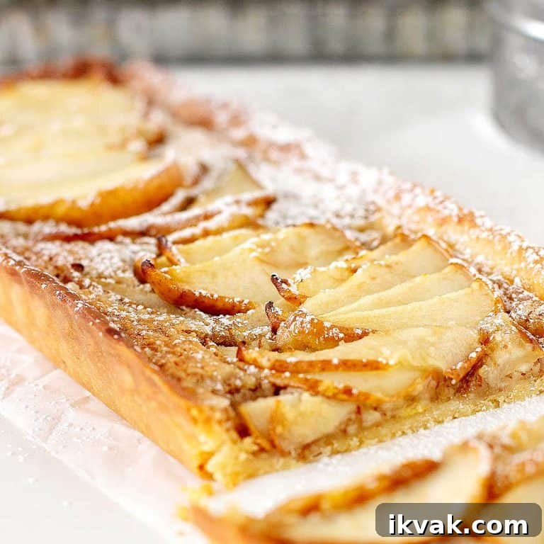 Close up of rectangular pear tart on a white surface with metal pan in the background.