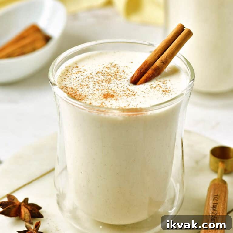 Glass of eggnog with cinnamon stick on a white board. Wooden spoon, anise stars.