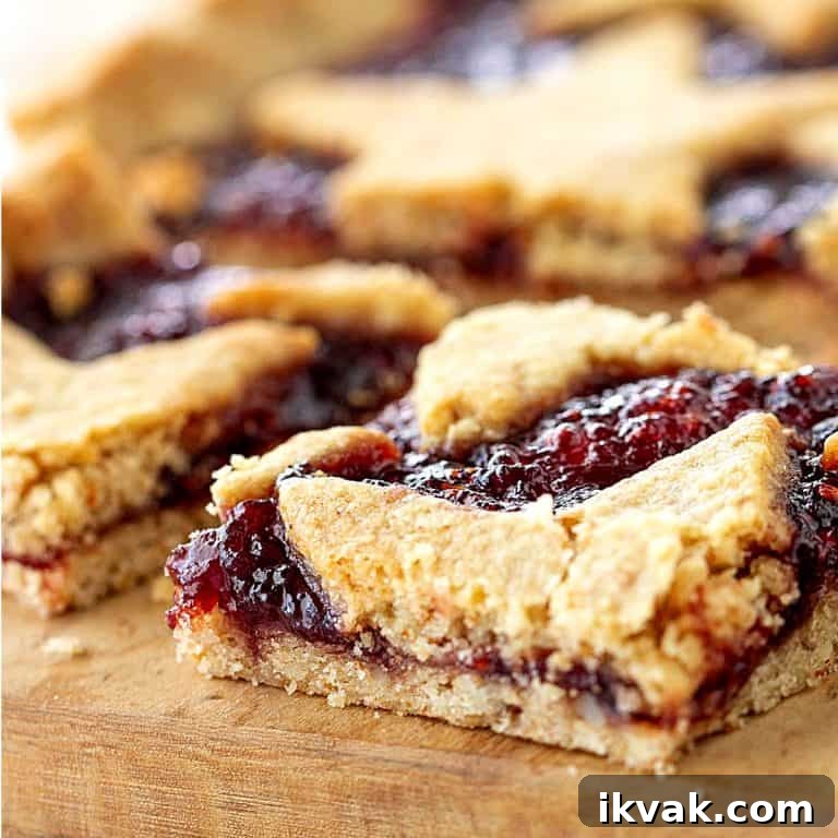 Crumbly squares of raspberry linzer tart on wooden board.
