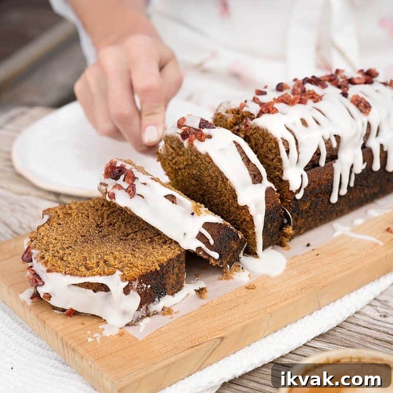 Glazed gingerbread loaf cake on a wooden board being sliced.