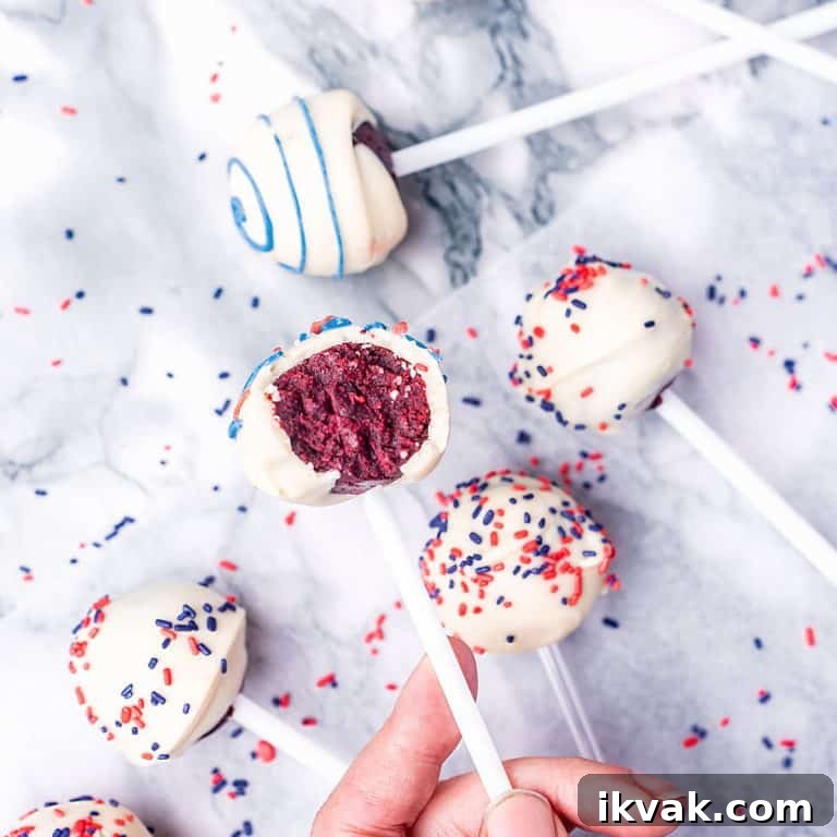 Bluish marble surface with several white chocolate red velvet cake pops with blue and red sprinkles and icing.
