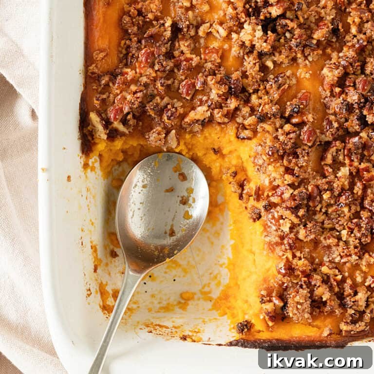 Close up of half eaten sweet potato pecan casserole on a white dish. Silver spoon inside.
