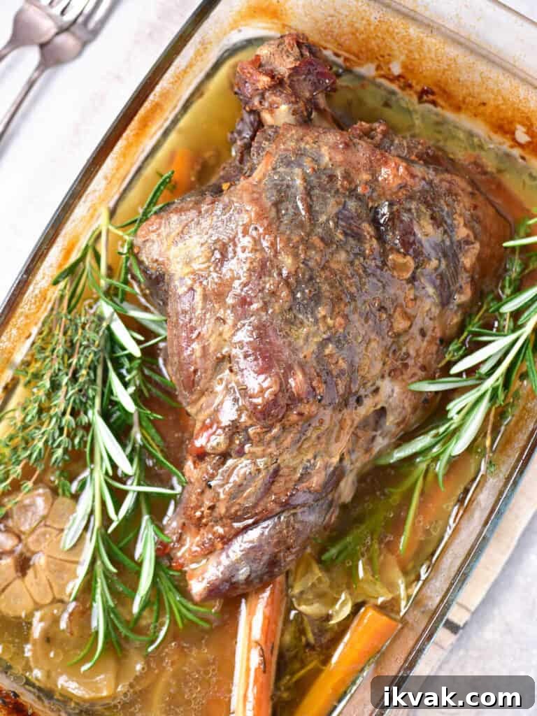 Whole slow roasted leg of lamb with fresh herbs on a glass dish.