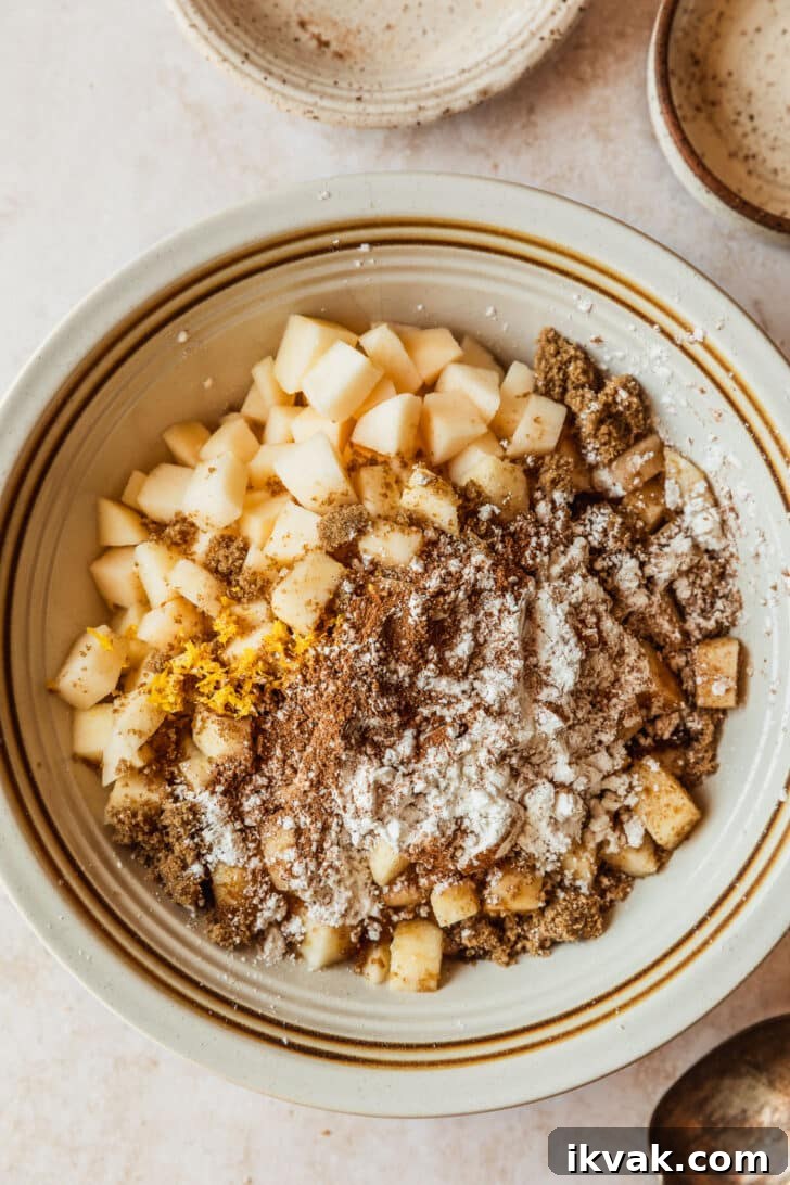 A white bowl with apples, brown sugar, & spices on a tan counter.