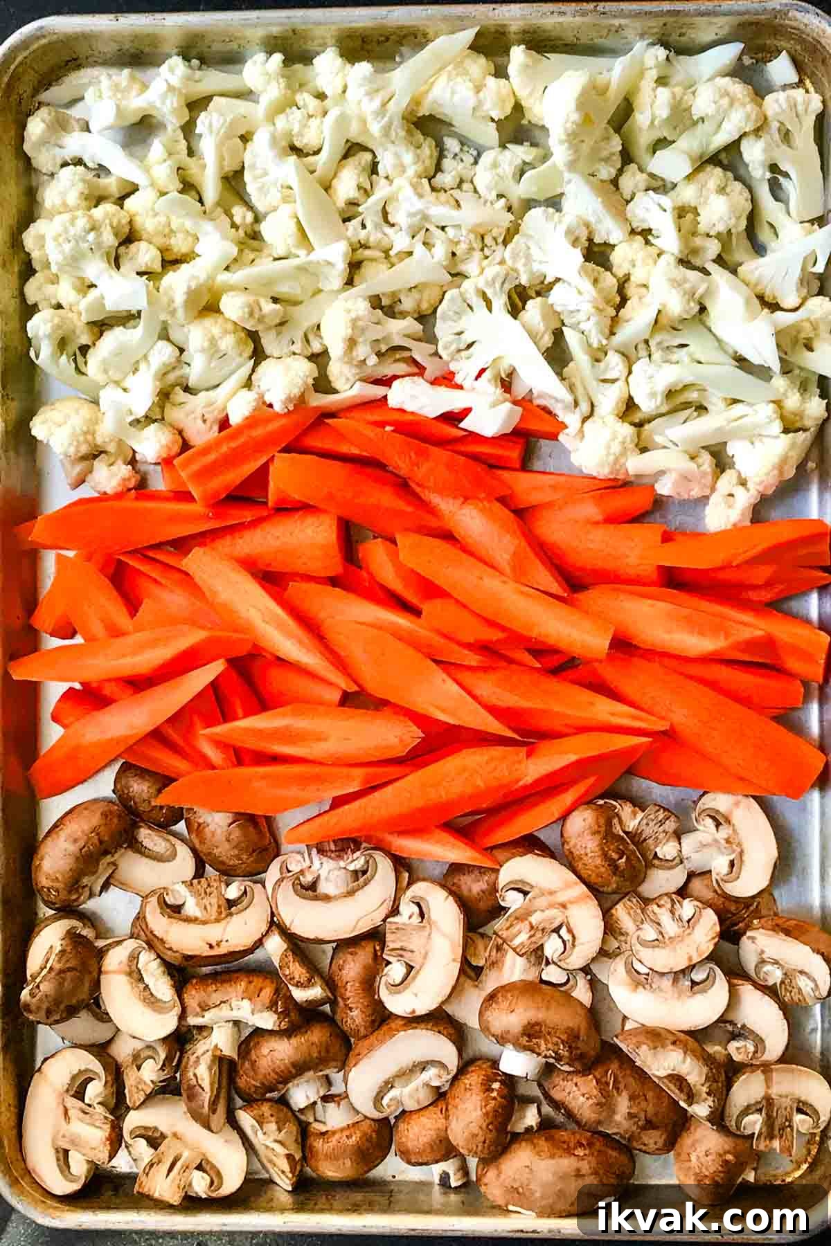 Rows of cauliflower florets, carrot spears and sliced mushrooms on a large rimmed baking sheet.