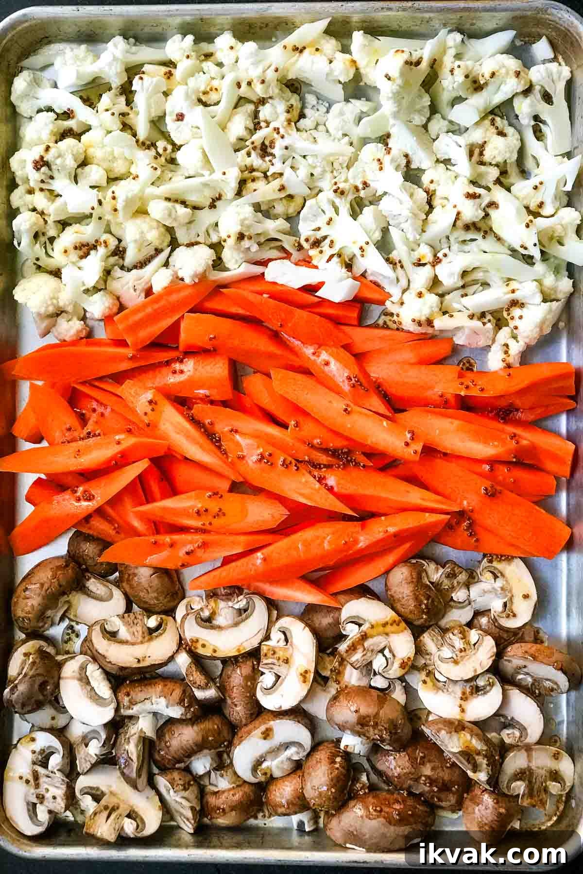 Baking tray with rows of cauliflower florets, spears of carrots and mushrooms drizzled with a mustardy dressing.