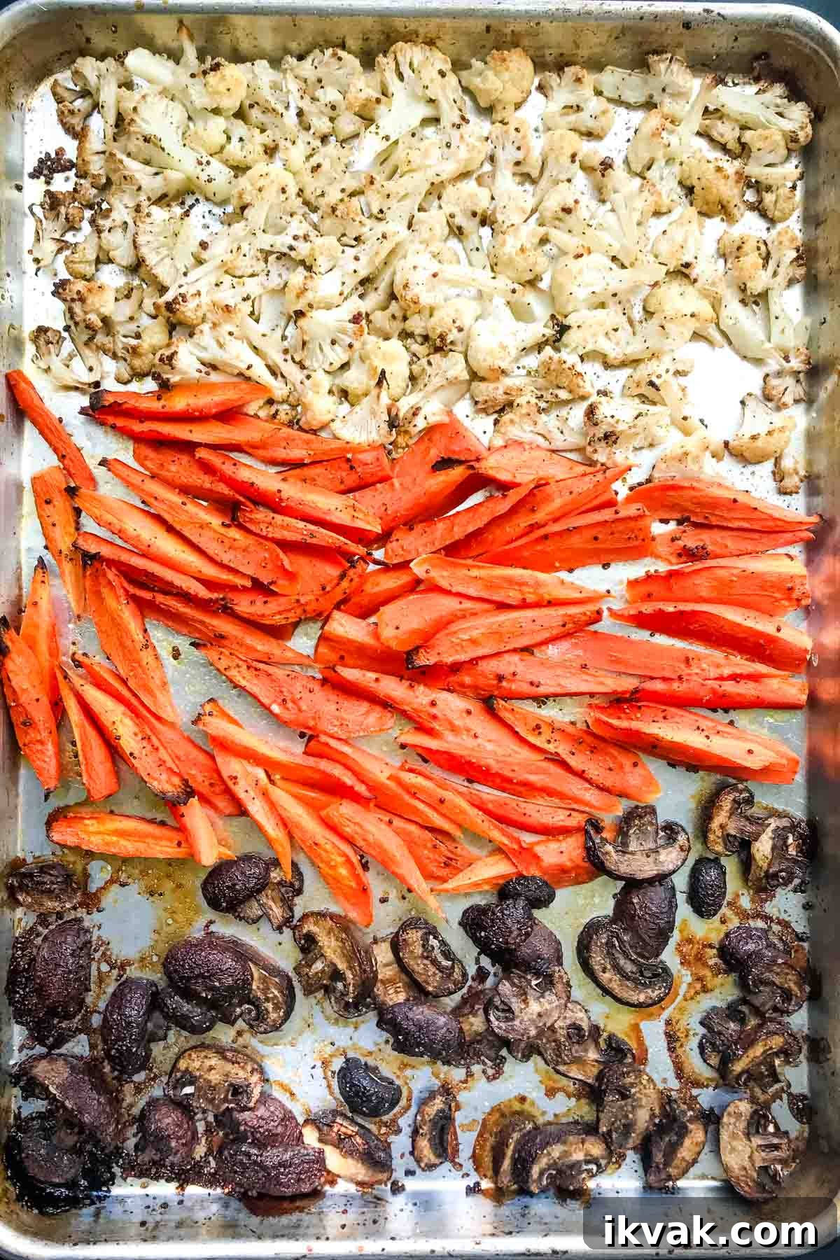 Roasted cauliflower florets, carrot spears and sliced mushrooms on a large rimmed baking tray.
