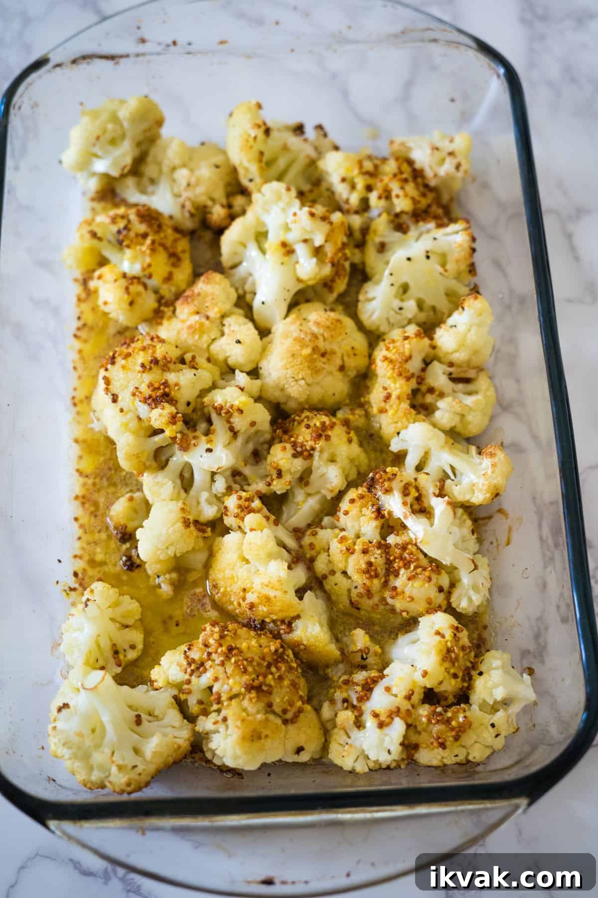 Keto roasted cauliflower with spices in a glass baking dish on a marble counter.