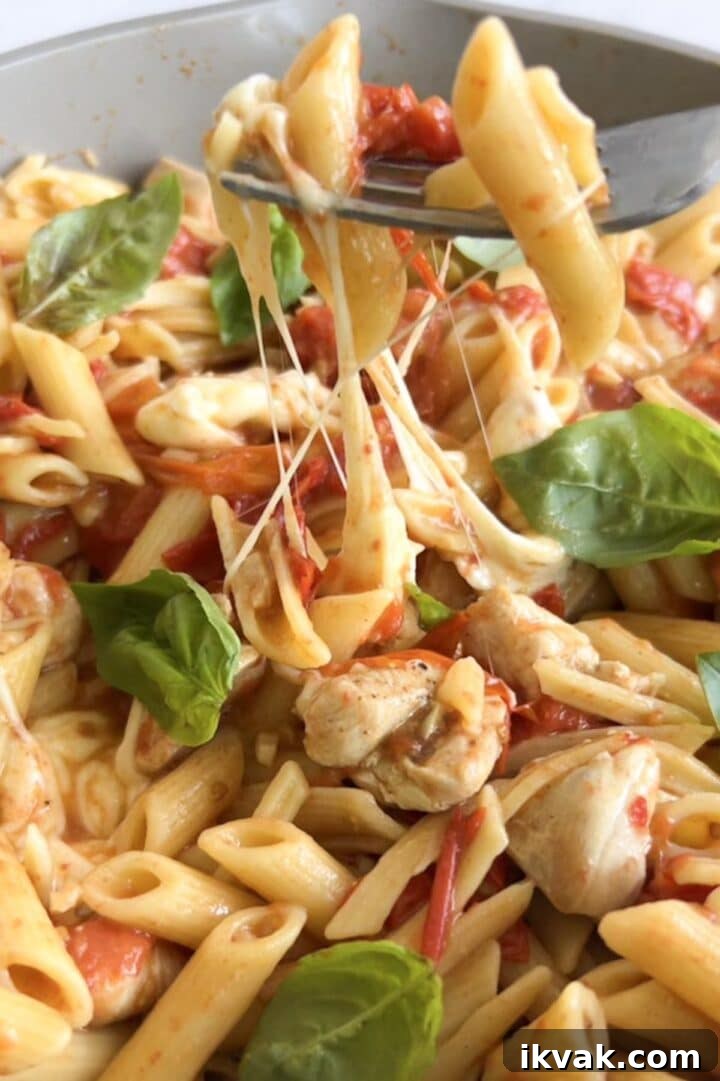 Gooey cheese pull in a large pan with balsamic chicken pasta