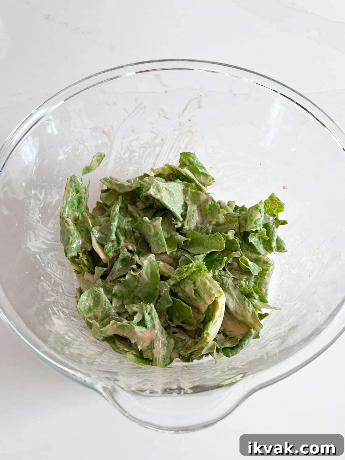 Lettuce covered in dressing in a glass bowl.