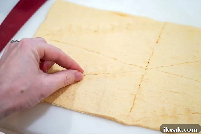 A hand pinching perforations on crescent rolls dough
