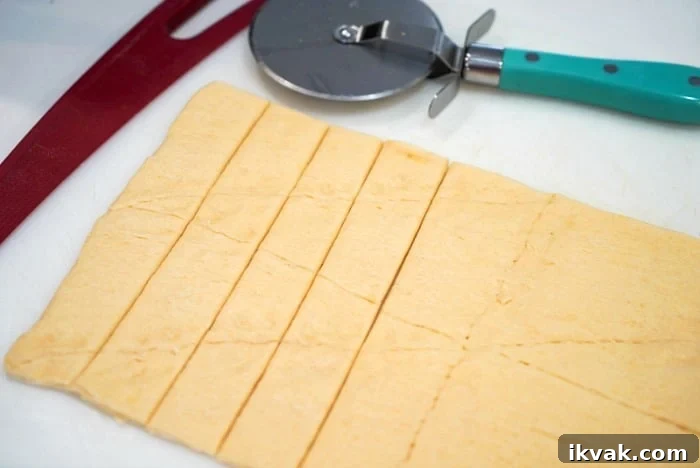 Rolled-out crescent roll dough sliced into strips with a pizza cutter