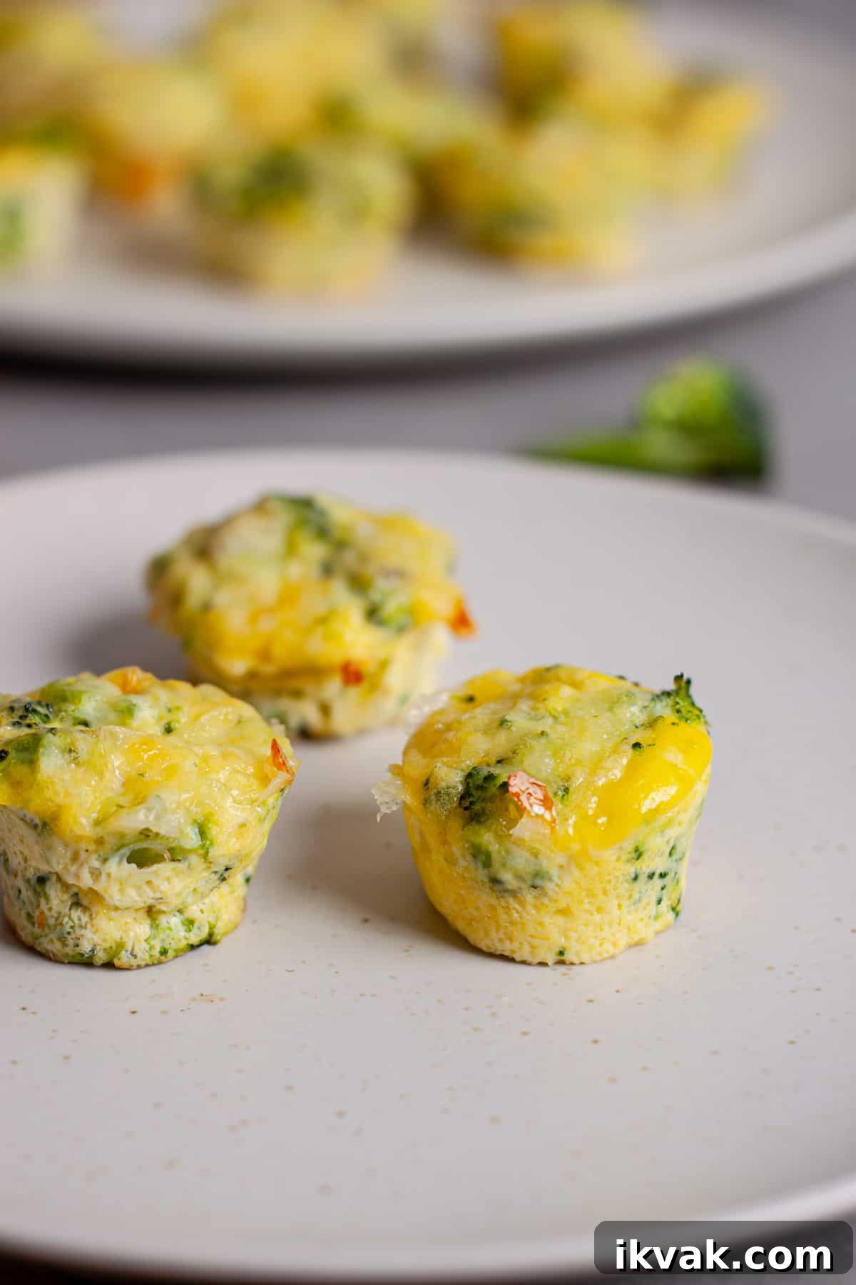 A small plate of mini broccoli and cheddar egg bites with more in the background.