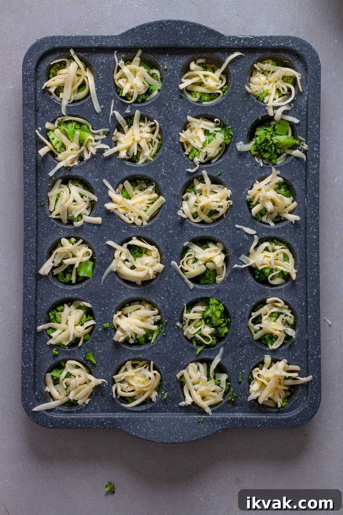 A mini muffin pan with shredded cheese and chopped broccoli.