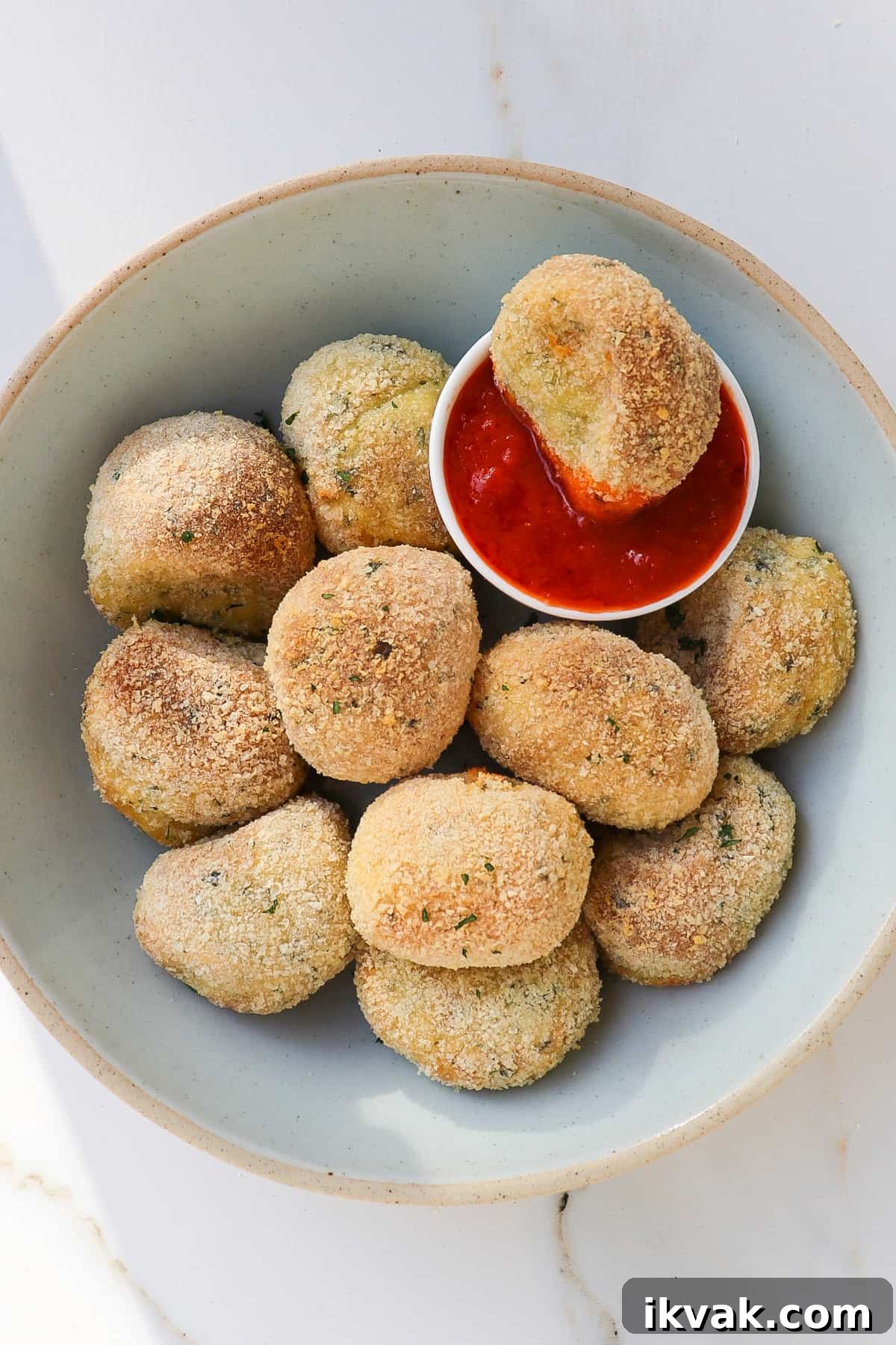 Crispy Air Fryer Potato Croquettes Recipe 11 Potato croquettes in a bowl with one dipped in marinara sauce.