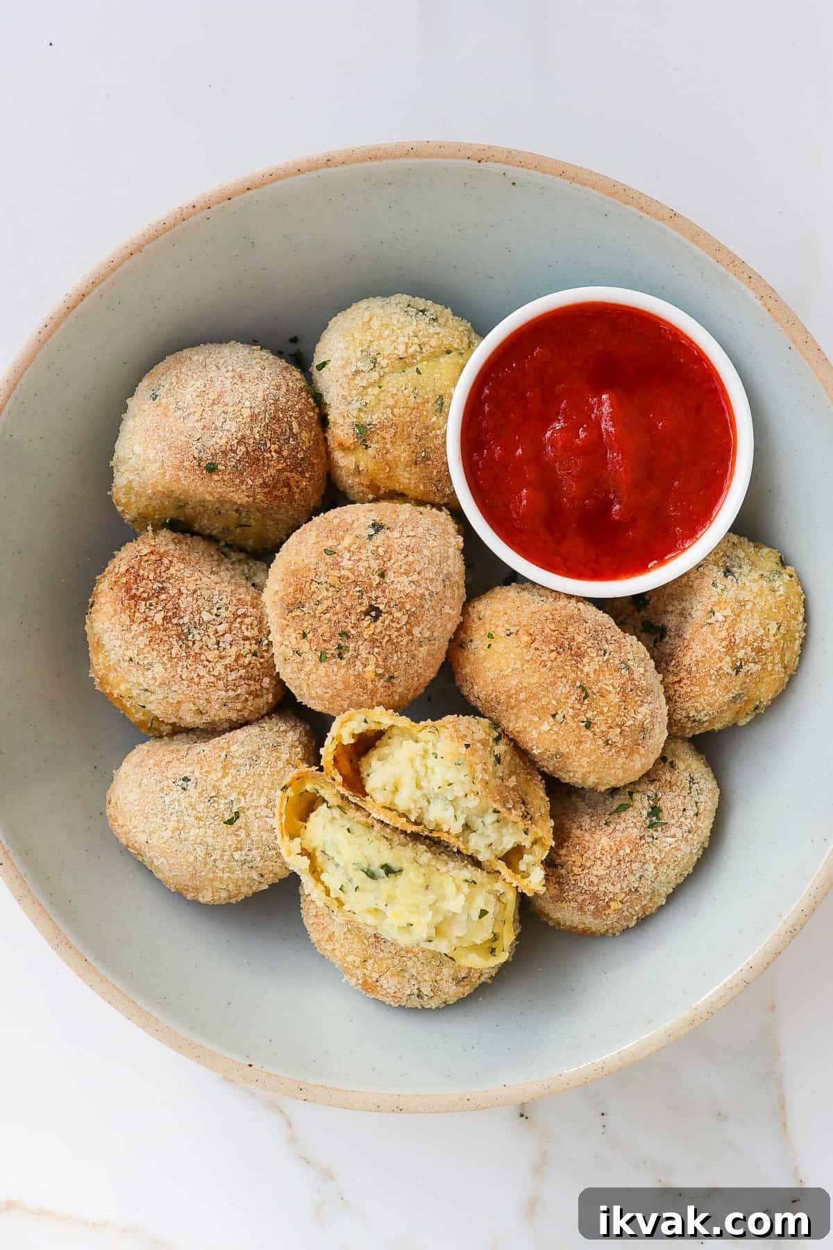 Crispy Air Fryer Potato Croquettes Recipe 9 Potato croquettes in a bowl with marinara sauce. One croquette open in half.