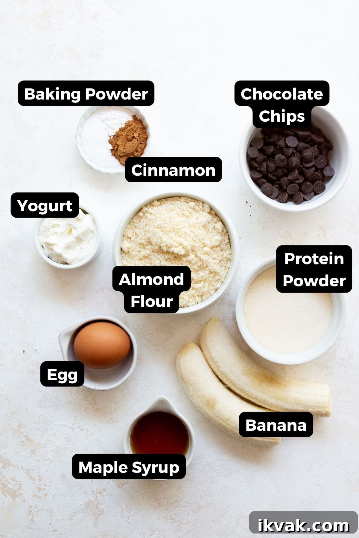 High-Protein Banana Muffins for Breakfast and Snacks 3 all ingredients in bowls including almond flour, protein powder, egg, yogurt, banana, maple syrup, egg, baking powder, and cinnamon