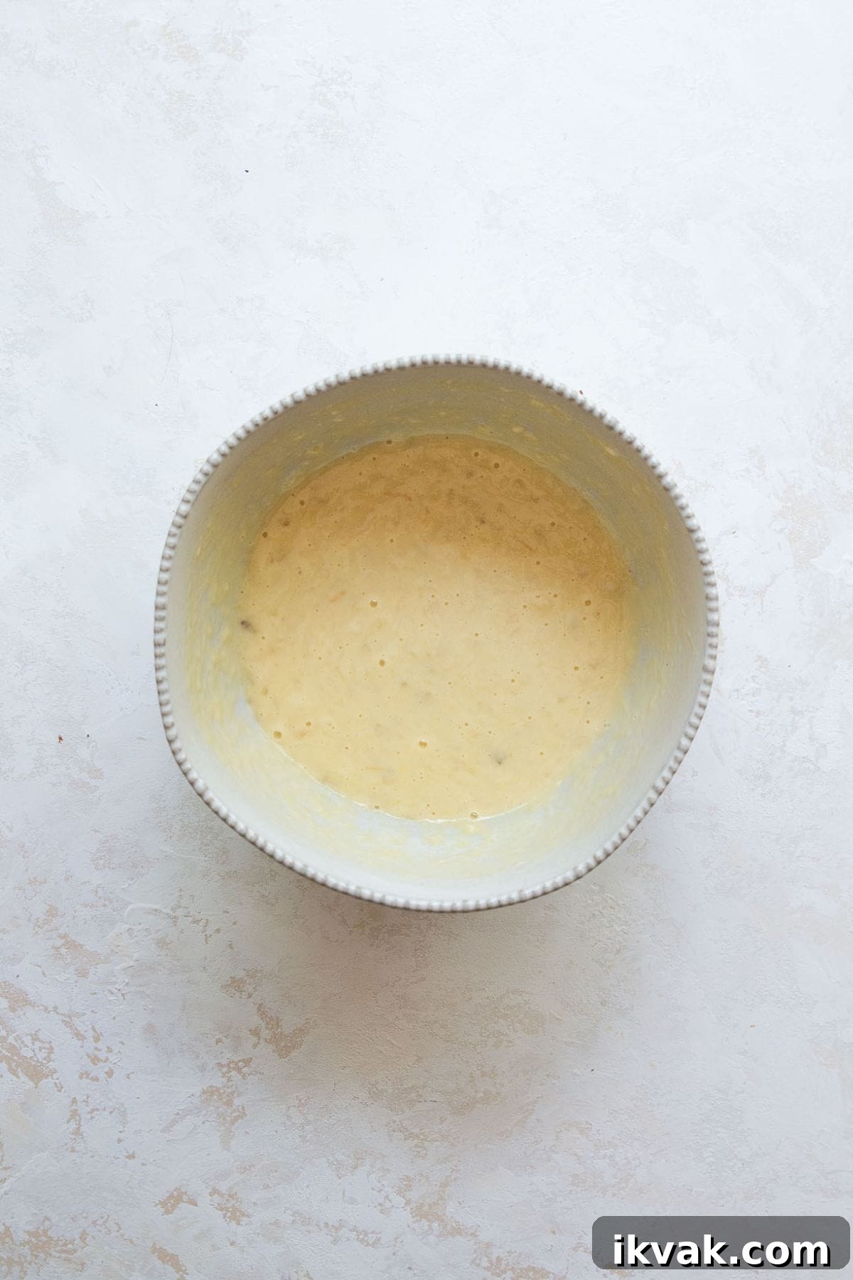 High-Protein Banana Muffins for Breakfast and Snacks 5 Wet ingredients for banana protein muffins whisked together in a bowl, including mashed bananas, Greek yogurt, egg, and honey.