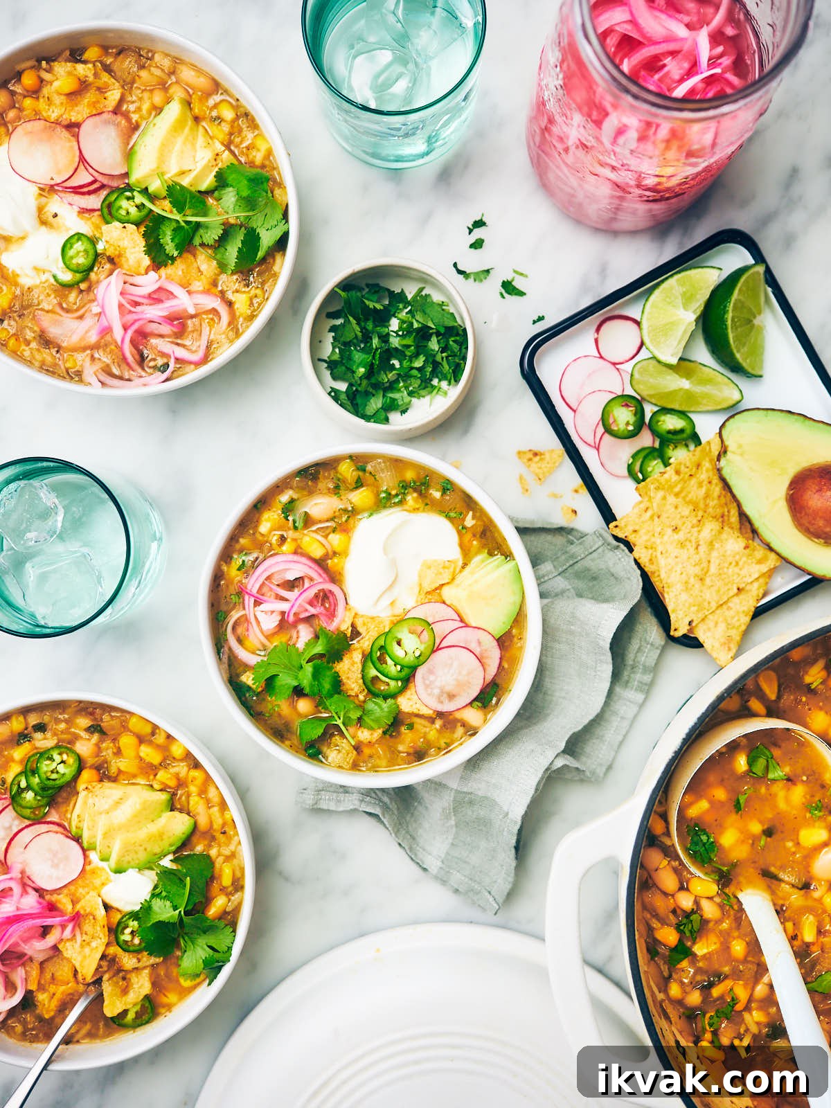 Green Chili Soup in bowls with toppings on a marble kitchen counter.