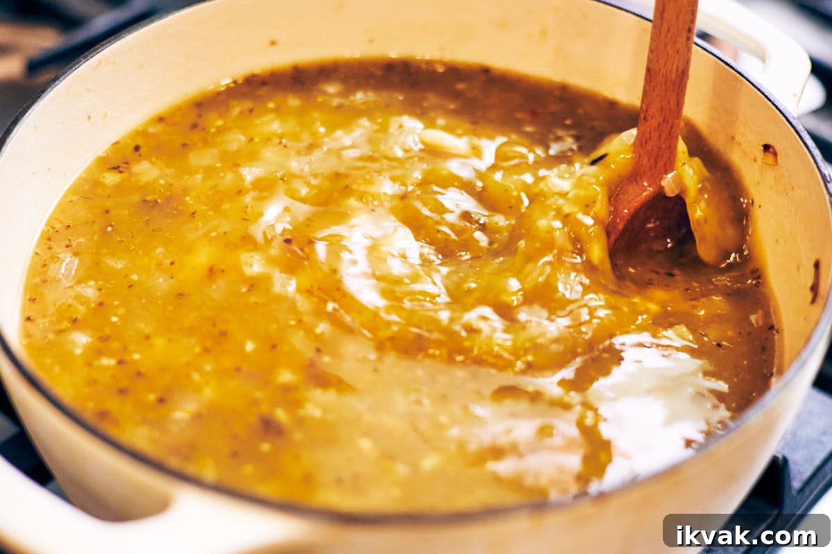 A wooden spoon stirring a pot of soup made with salsa verde and rice.