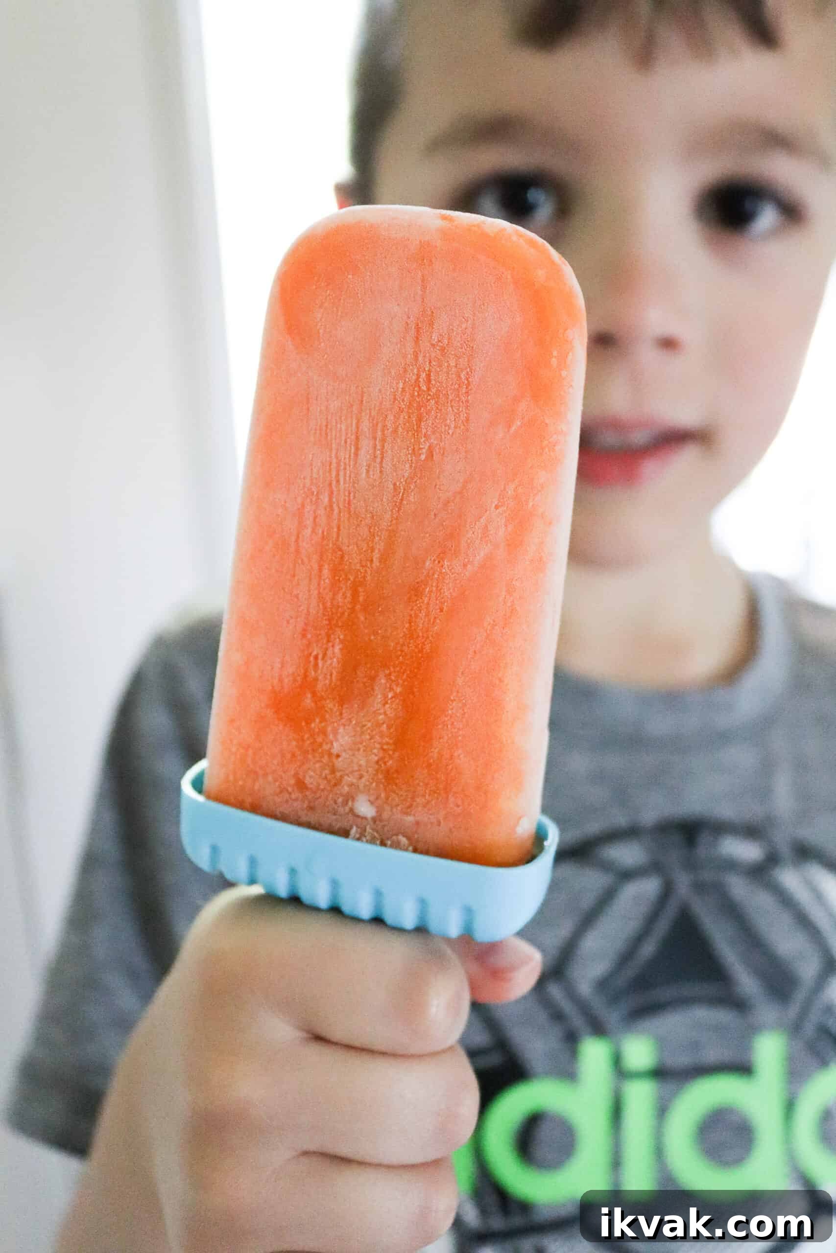 homemade orange popsicle kid holding homemade orange popsicle with no added sugar