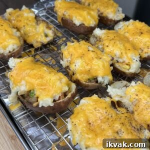 Shepherd's Pie Stuffed Twice-Baked Potatoes 35 A tray of Shepherd's Pie Twice Baked Potatoes with melted cheddar cheese and seasoning rests on a wire rack in a kitchen. The potato halves are stuffed and slightly overflowing with a creamy, flavorful filling.