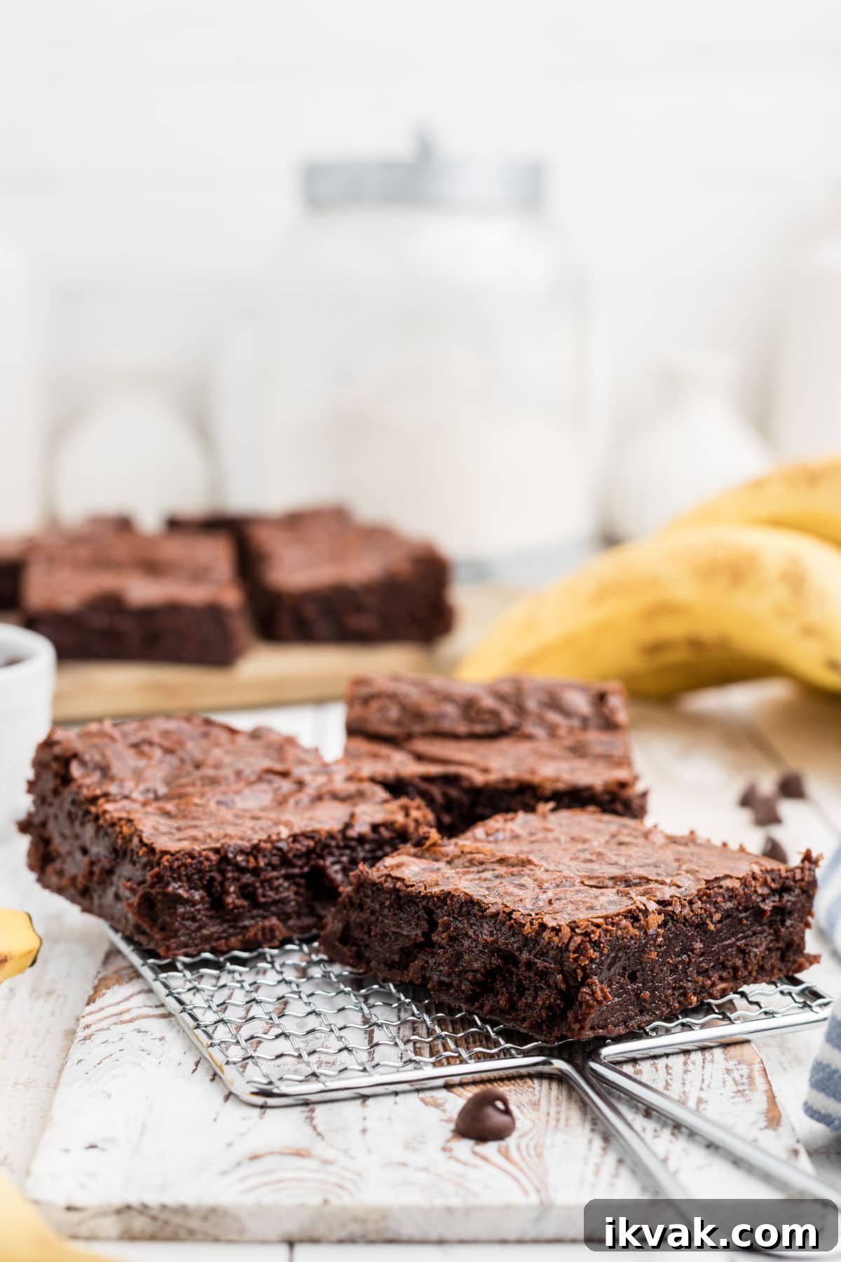 a small rack holding three banana brownies with a few bananas in the background