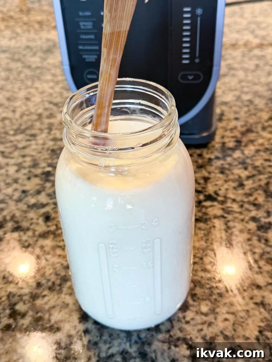 Ninja Slushy Mudslide Recipe: Frozen Coffee Cocktail Guide 4 A glass mason jar filled with creamy mudslide mixture and a wooden spoon inside, sitting on a granite countertop in front of a Ninja Creami machine.