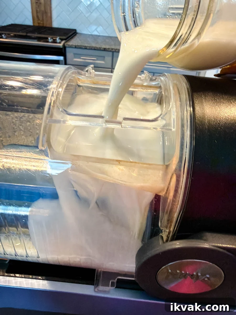 Ninja Slushy Mudslide Recipe: Frozen Coffee Cocktail Guide 5 Creamy mudslide mixture being poured from a jar into the Ninja Creami container, showing the smooth liquid filling up the machine insert with a kitchen stove and backsplash in the background.