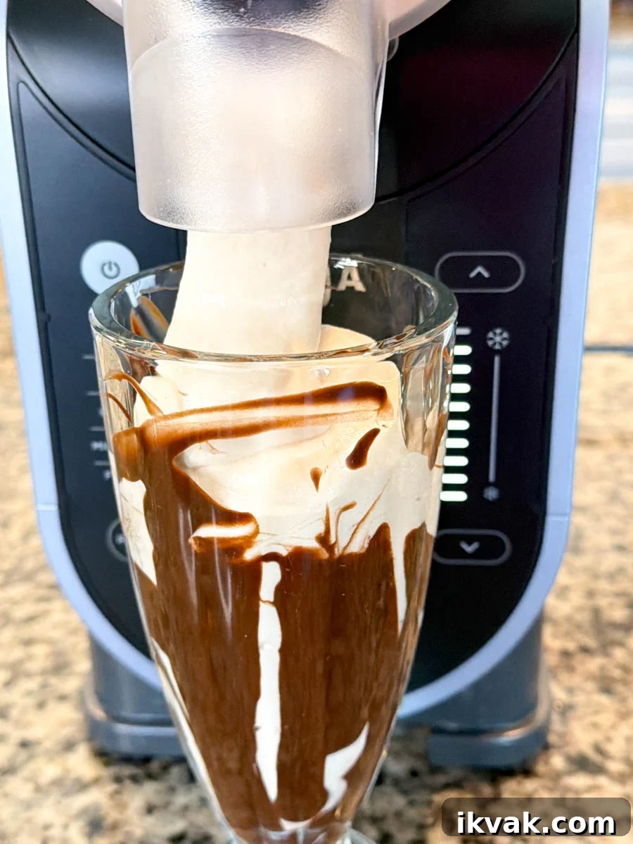 Ninja Slushy Mudslide Recipe: Frozen Coffee Cocktail Guide 7 Close-up of a Ninja Creami machine dispensing a thick, creamy mudslide mixture into a tall glass lined with chocolate syrup, showing the texture as it pours out smoothly.