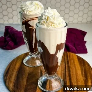Ninja Slushy Mudslide Recipe: Frozen Coffee Cocktail Guide 9 Two tall glasses filled with creamy Ninja Slushi Mudslides swirled with chocolate syrup and topped with whipped cream, placed on a wooden board with a purple cloth in the background.