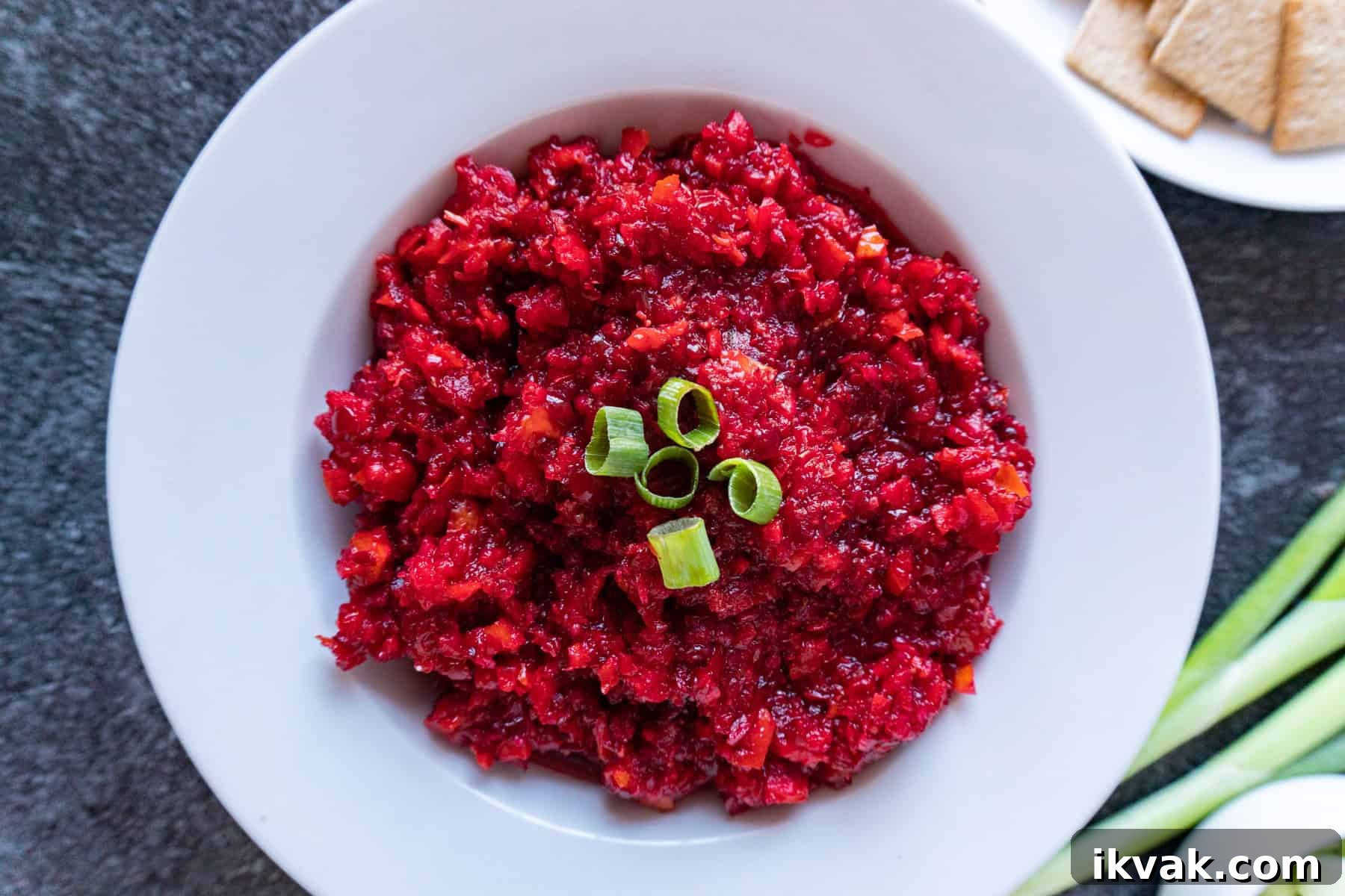 Zesty Cranberry Relish Recipe for Holiday Tables 7 cranberry relish in a white bowl garnished with green onions.