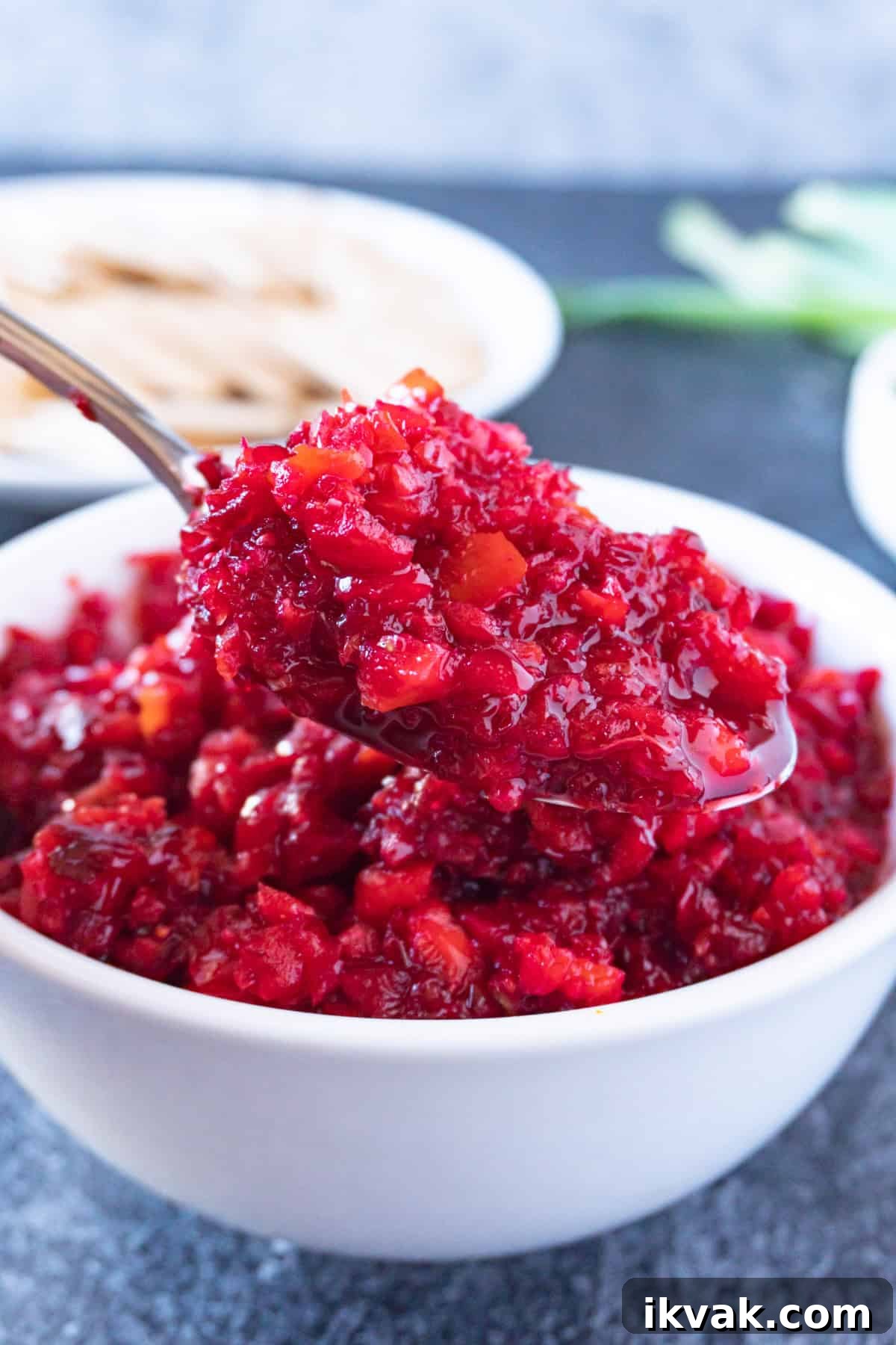 Zesty Cranberry Relish Recipe for Holiday Tables 8 scooping cranberry relish out of a white bowl with a spoon.