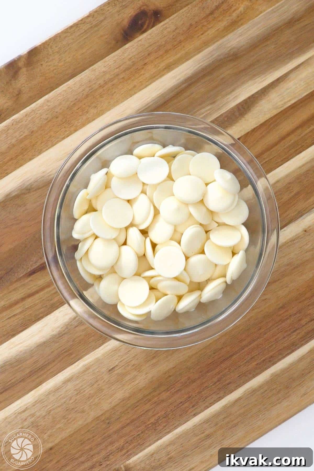 Glass bowl of white candy coating wafers on a wooden cutting board.