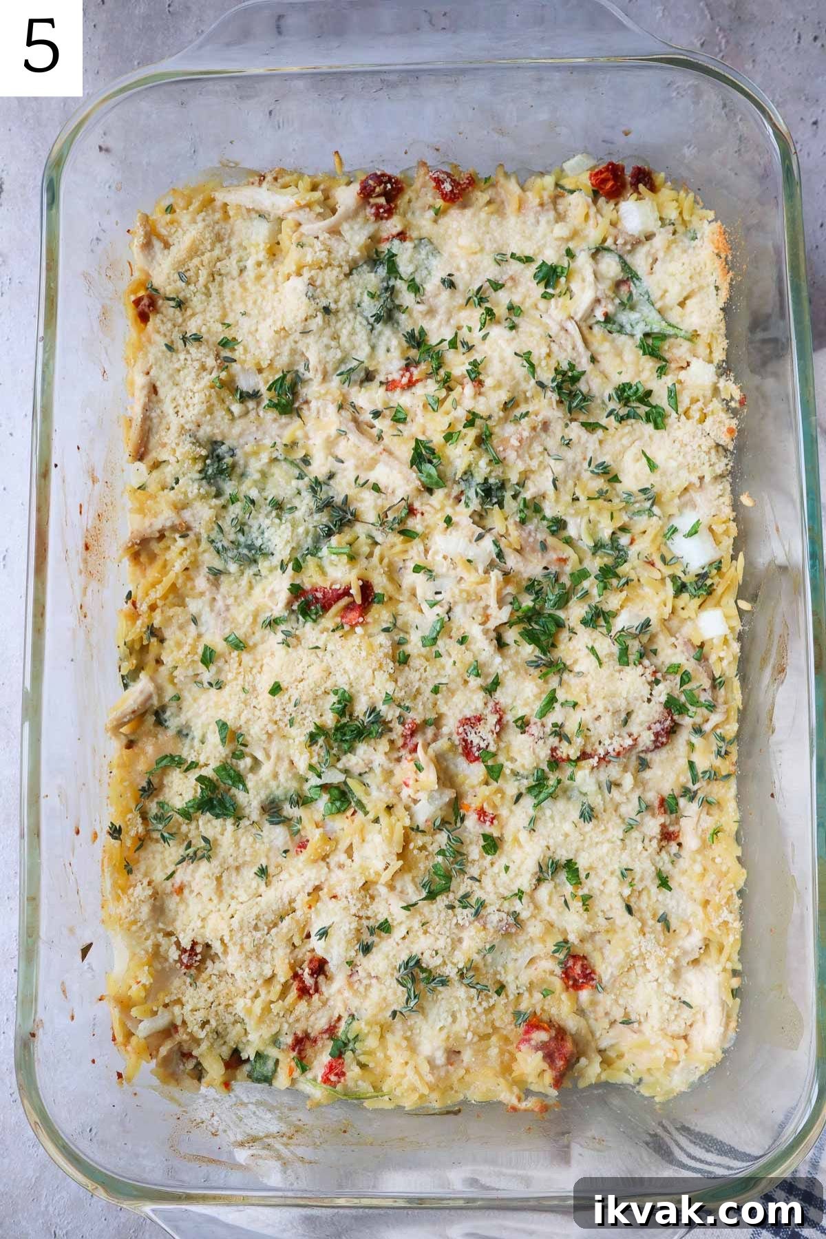 glass baking dish with creamy chicken orzo bake topped with parsley.