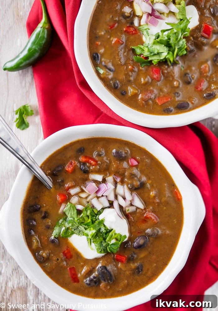 Two bowls of black bean soup topped with sour cream and chopped cilantro.