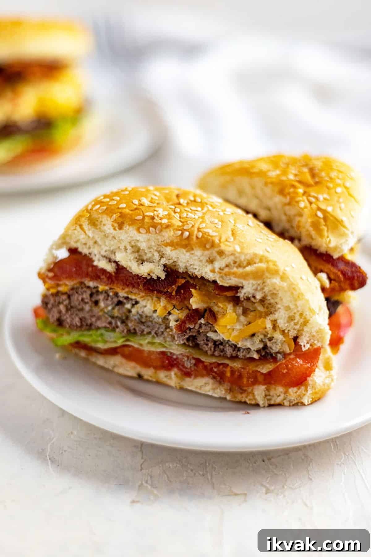 cut in half cheesy stuffed burger topped with bacon and pimento cheese and lettuce and tomato on white plate