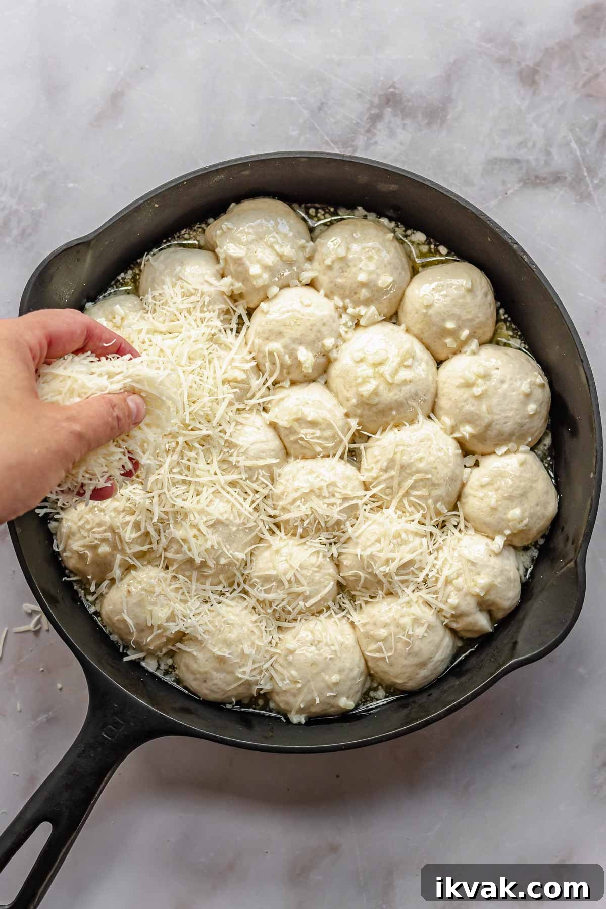 A hand scatters shredded parmesan cheese on top of pre-baked bread bites.