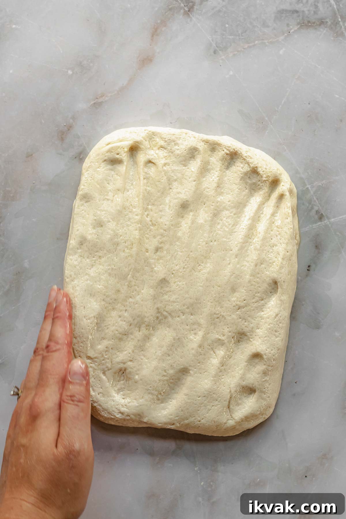 A hand forms the pizza dough into a rectangle.