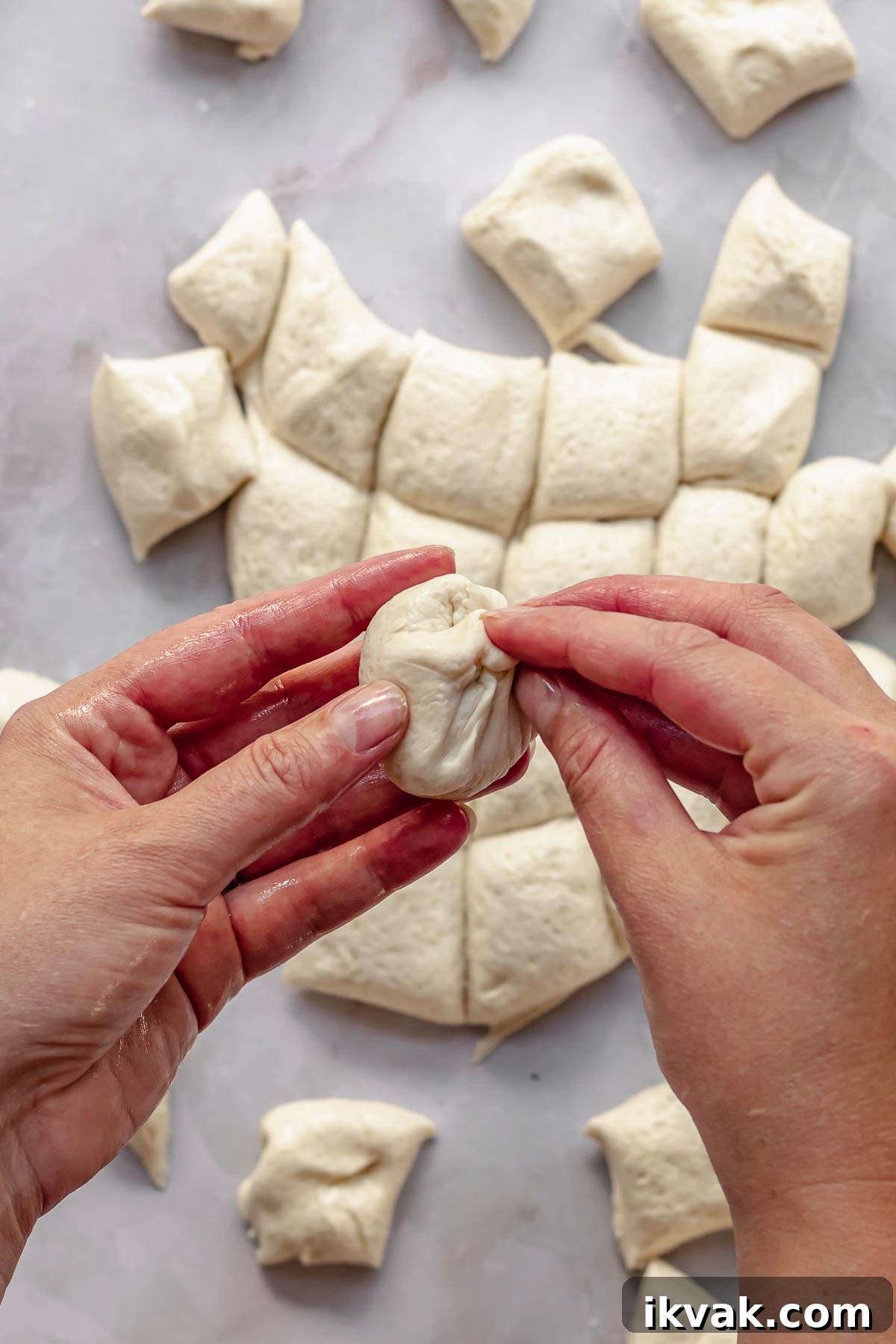 Hands pinch pizza dough into a round ball.