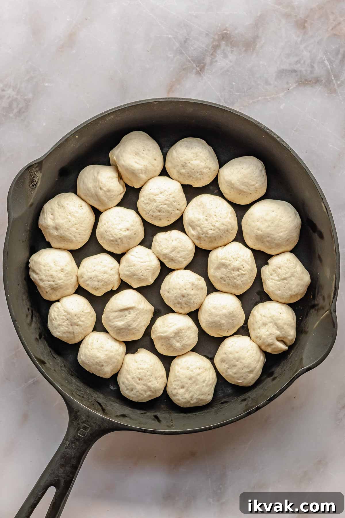 Round balls of pizza dough fill a cast iron skillet.