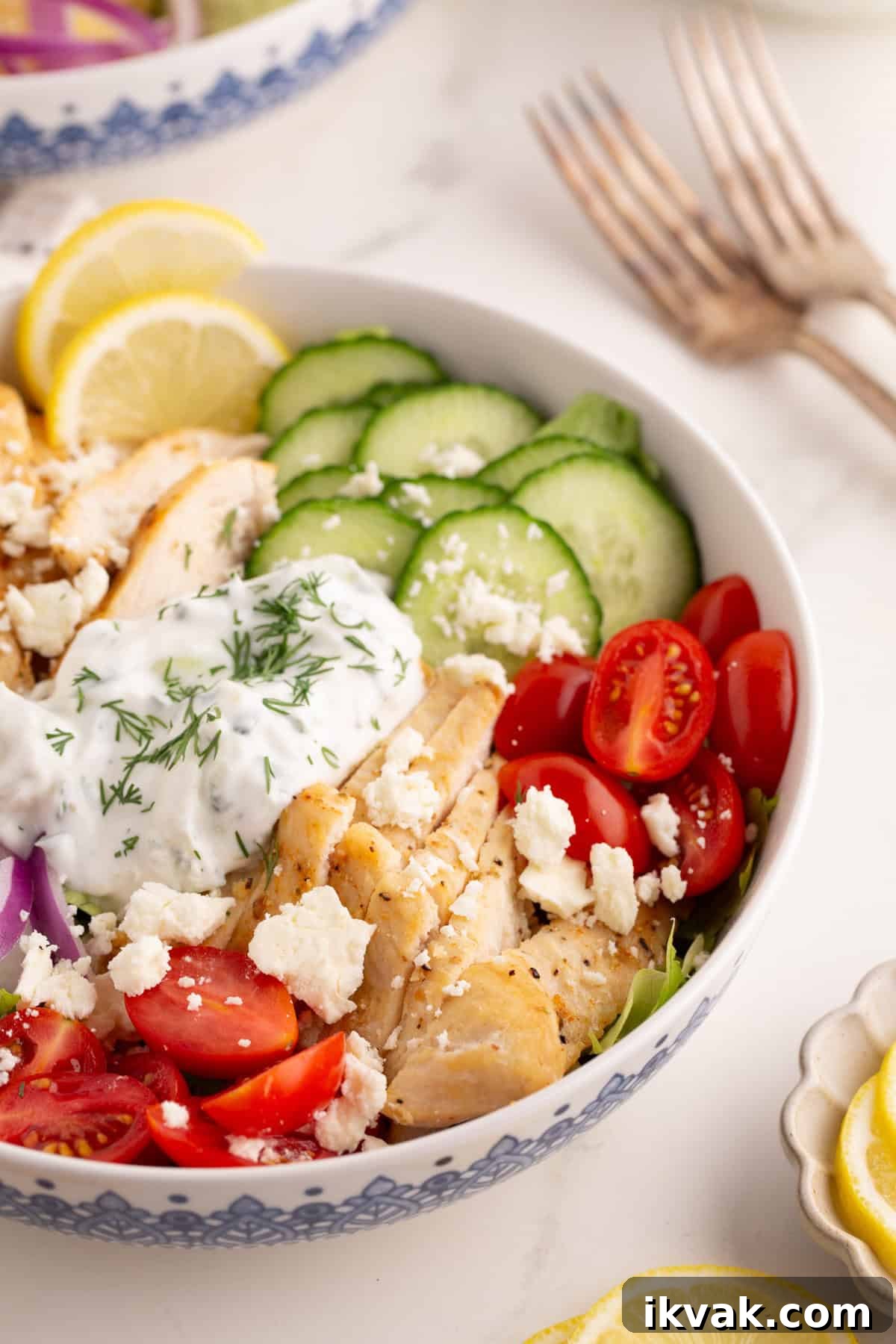 Chicken gyro bowl with sliced vegetables, tzatziki sauce, and lemon slices.