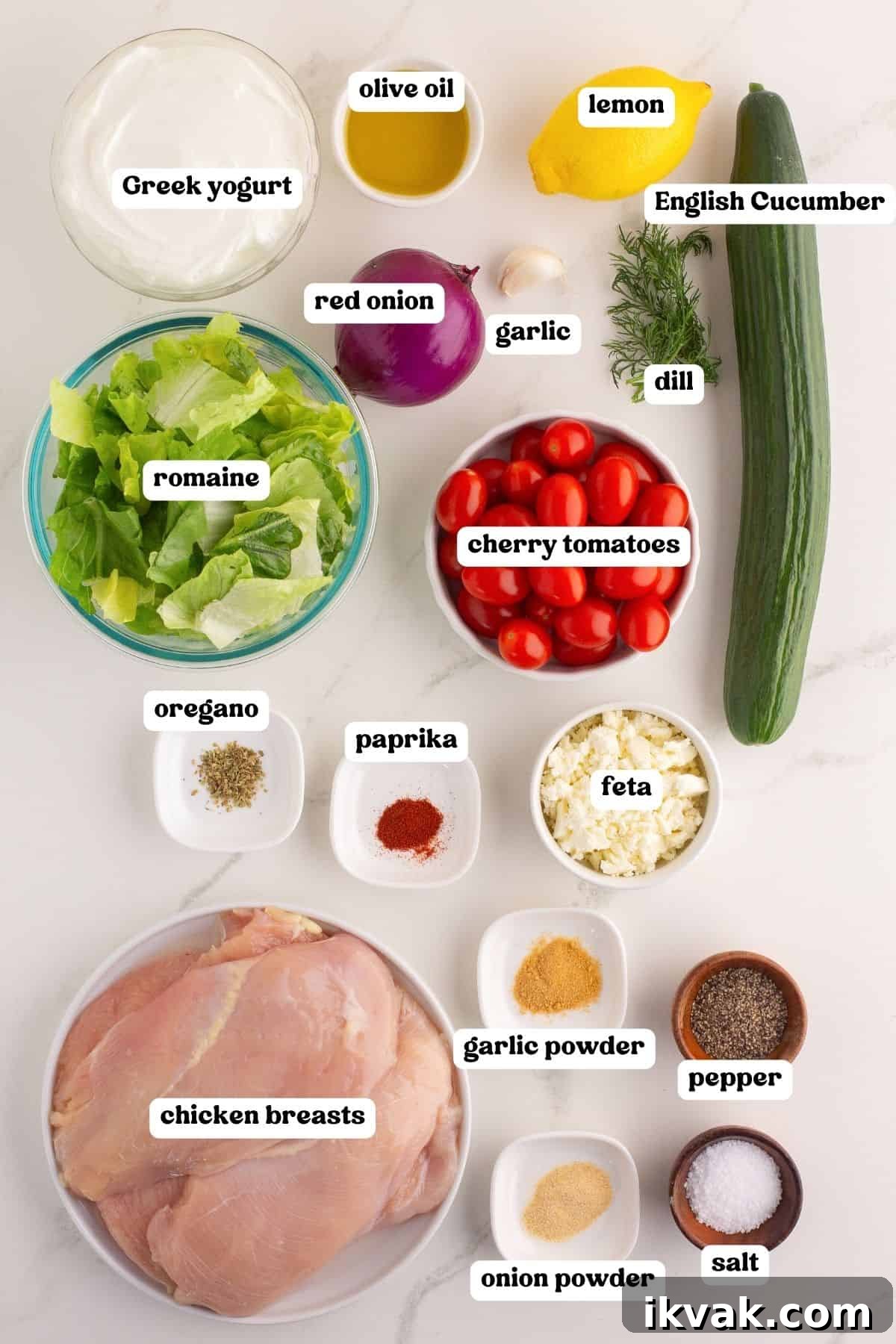 Image showing all ingredients for Greek chicken gyro bowls, each labeled with white text. Ingredients include Greek yogurt, olive oil, lemon, English cucumber, red onion, garlic, dill, cherry tomatoes, romaine, oregano, paprika, feta, chicken breasts, garlic powder, onion powder, pepper, and salt.