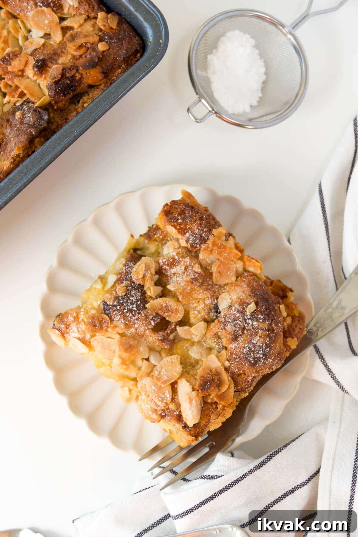 Decadent Panettone Bread Pudding Recipe for Holiday Brunch 2 a slice of panettone bread pudding on a white scalloped plate with a fork next to a square pan of more bread pudding