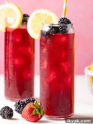 two glasses of berry lemonade garnished with lemon and blackberries.