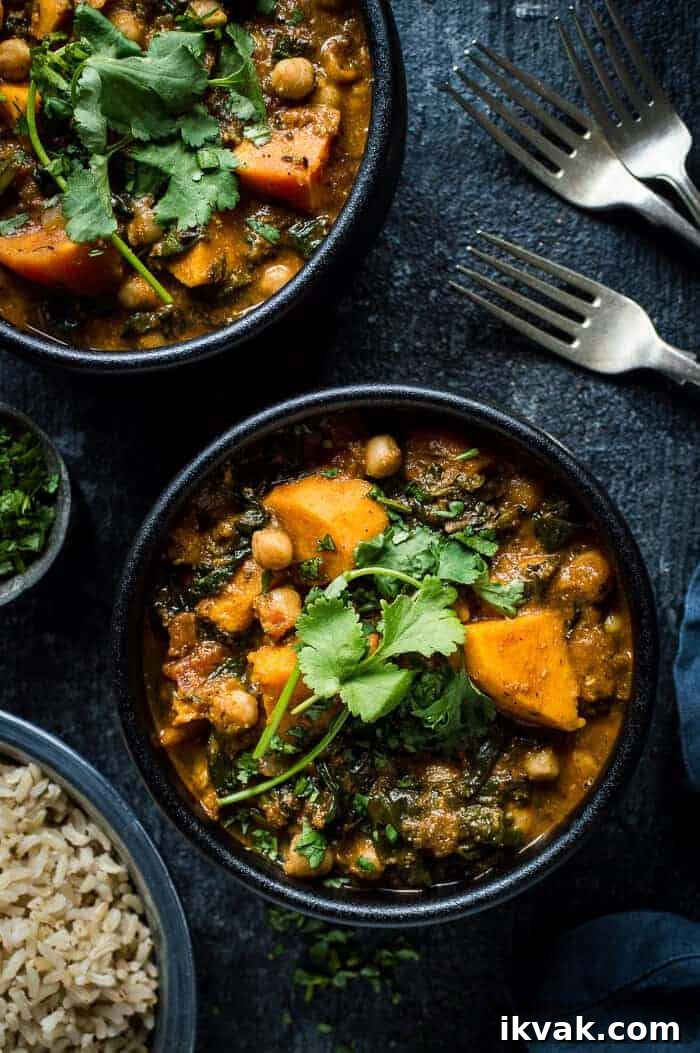 Two black bowls of vegan chickpea, sweet potato and spinach curry on a black background.