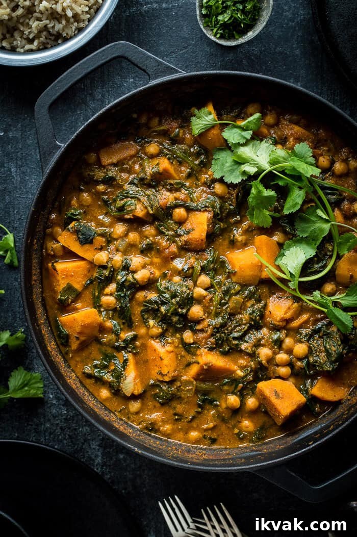 Close up of a black pan of vegan chickpea, sweet potato and spinach curry topped with fresh coriander.