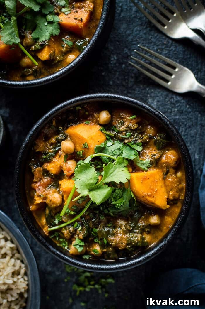 Close up of vegan chickpea, sweet potato and spinach curry in a black bowl on a black background.