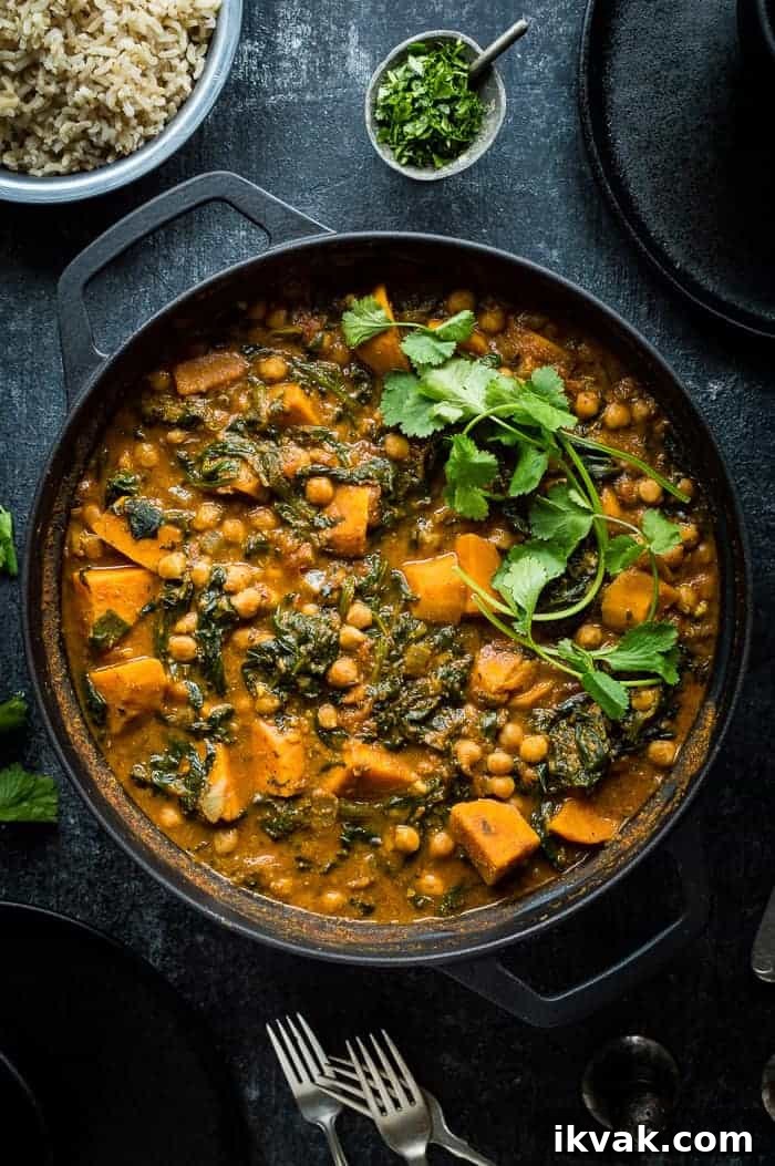 Plant based chickpea, sweet potato and spinach curry in a black cast iron pan on a black background.